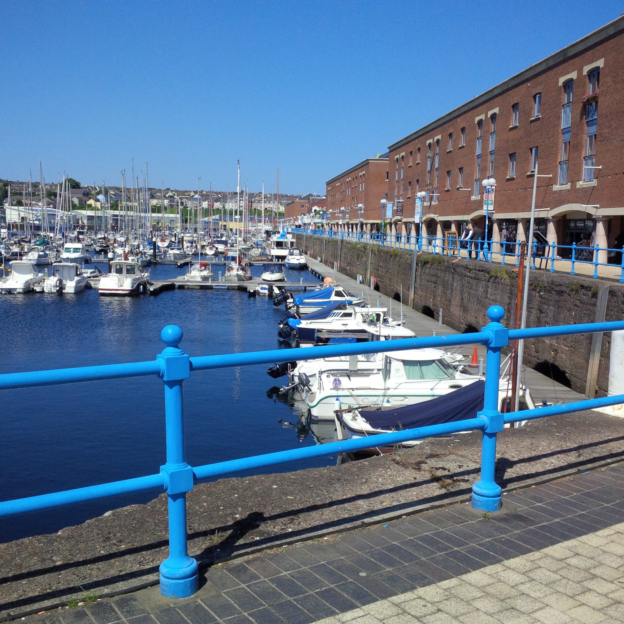 Milford marina in the sunshine showing boats in the forefront and a variety of shops and cafes alongside